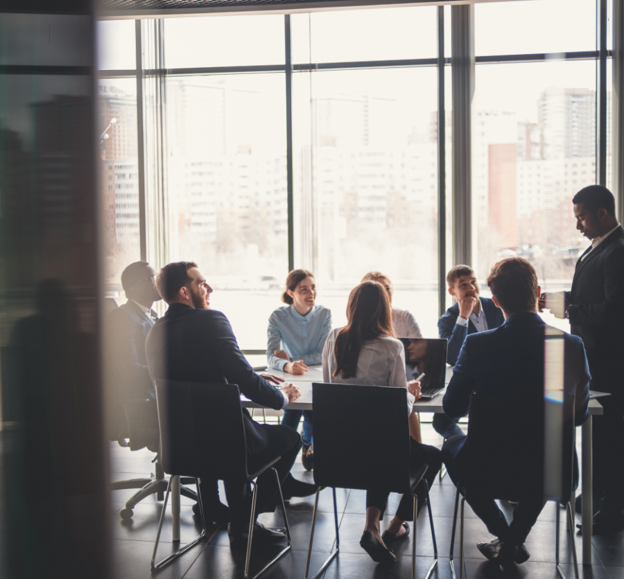 Image of a group of business professionals in a meeting, with one person standing and giving a presentation to the team.