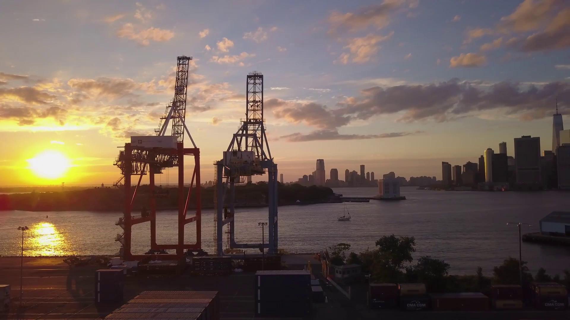 Sunset view of The Port of New York and New Jersey with shipping containers and cranes silhouetted against the sky.